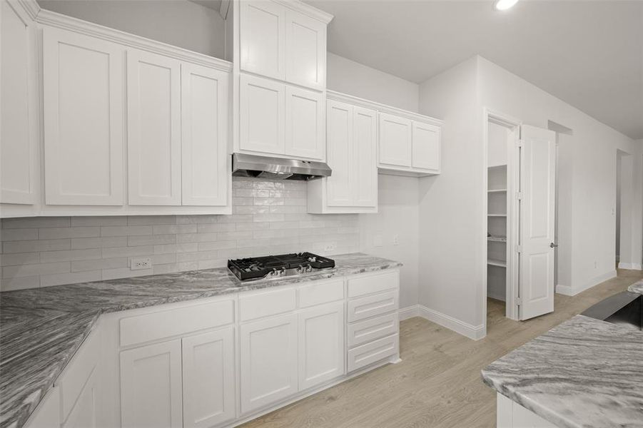Kitchen with exhaust hood, stainless steel gas cooktop, white cabinets, and light wood-type flooring Kitchen with exhaust hood, stainless steel gas cooktop, white cabinets, and light wood-type flooring