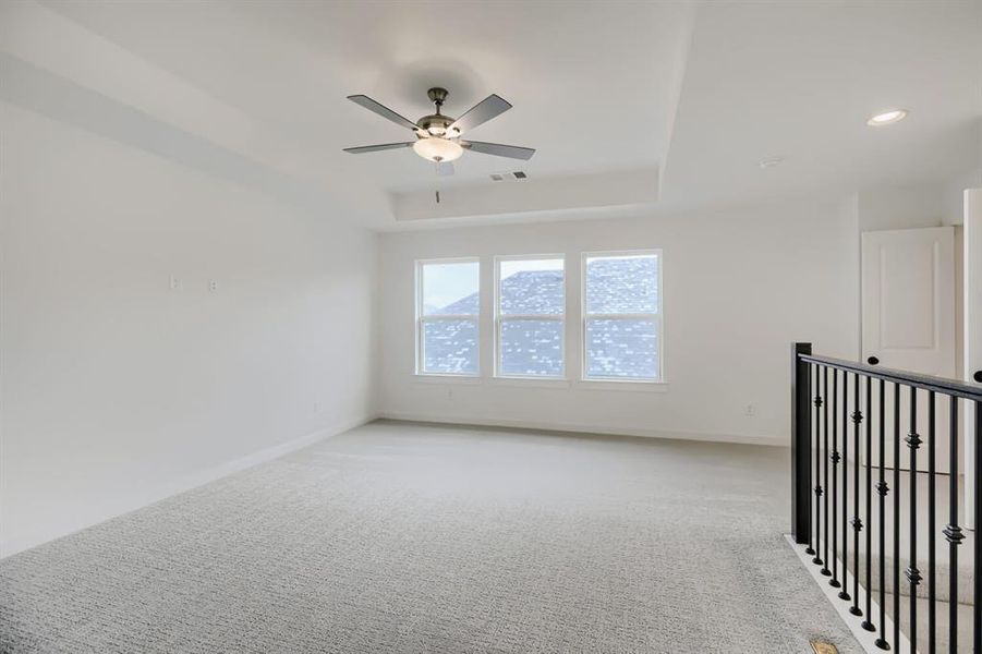 Empty room with carpet floors, a ceiling fan, and a tray ceiling