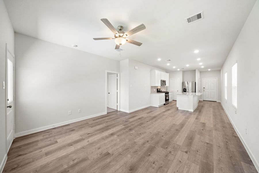 A large empty room with a ceiling fan and wood floors.