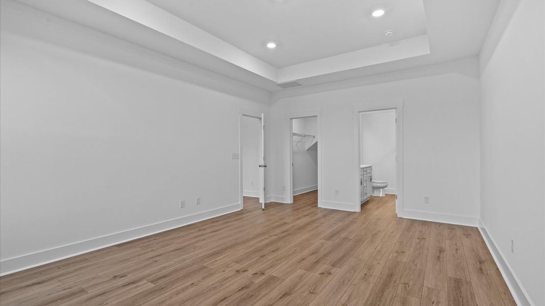 Elegant primary suite with hardwood flooring, tray ceiling, and superior natural light in this accomplished DRB Homes design