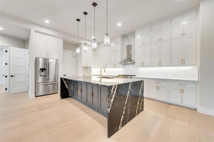 Kitchen with stainless steel fridge, wall chimney exhaust hood, a sink, white cabinets, and recessed lighting Kitchen with stainless steel fridge, wall chimney exhaust hood, a sink, white cabinets, and recessed lighting