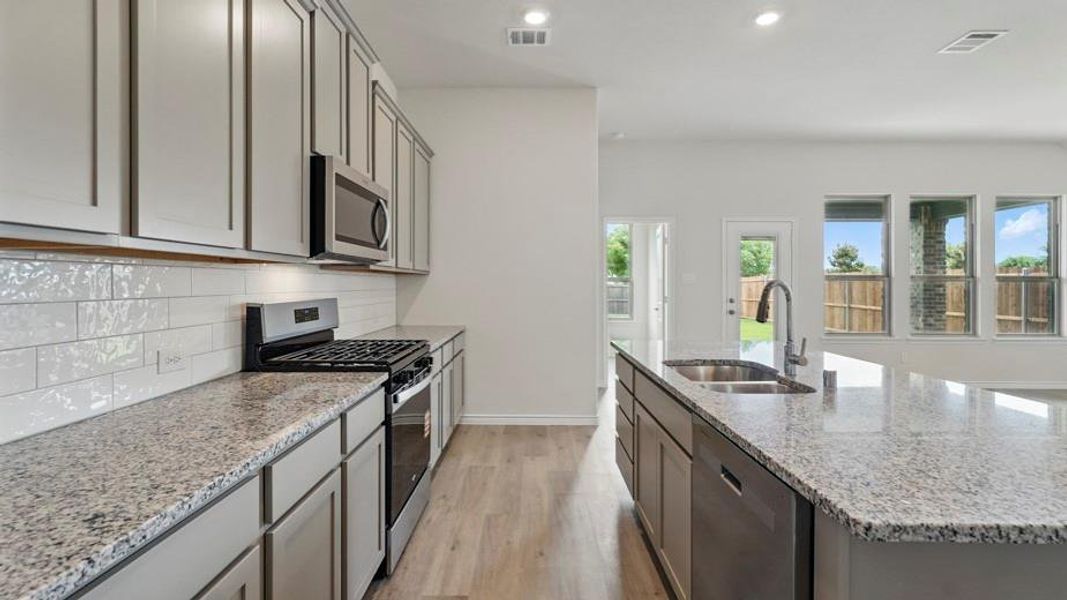 Kitchen with gray cabinetry, stainless steel appliances, light stone countertops, a center island with sink, and recessed lighting