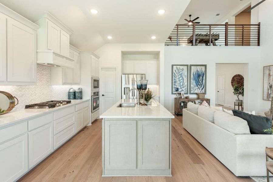 Open-concept kitchen with white cabinets, large island, and hardwood floors flowing into living area with second-floor loft above Open-concept kitchen with white cabinets, large island, and hardwood floors flowing into living area with second-floor loft above