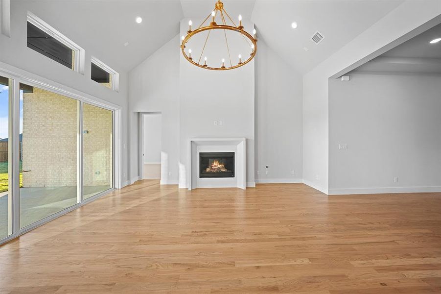 Unfurnished living room featuring high vaulted ceiling, light wood-style flooring, a chandelier, a glass covered fireplace, and recessed lighting Unfurnished living room featuring high vaulted ceiling, light wood-style flooring, a chandelier, a glass covered fireplace, and recessed lighting