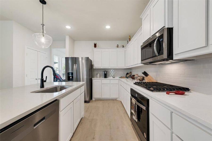 Kitchen featuring decorative light fixtures, stainless steel appliances, light stone counters, white cabinets, and recessed lighting Kitchen featuring decorative light fixtures, stainless steel appliances, light stone counters, white cabinets, and recessed lighting