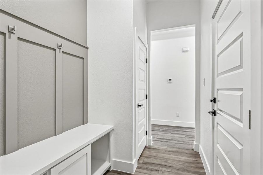 Entryway featuring a built-in bench with storage, board and batten wall paneling with hooks, white five-panel doors, and wood-finish flooring