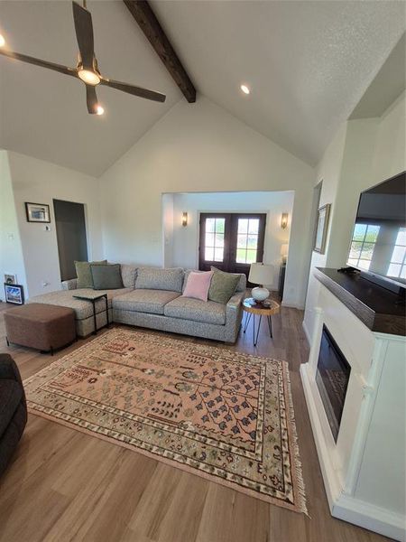Living room featuring high vaulted ceiling, wood finished floors, a glass covered fireplace, recessed lighting, and beamed ceiling