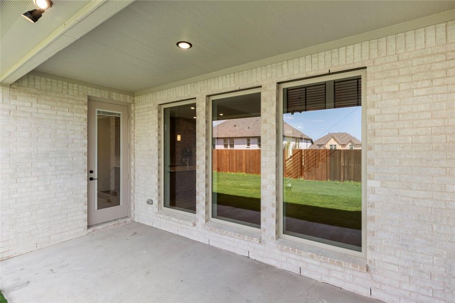 Covered back patio with concrete floor, brick exterior wall, large windows, and door leading inside