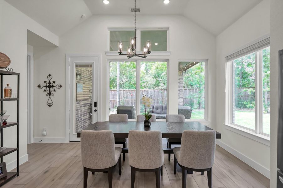 Bright dining area surrounded by large windows and upgraded lighting, offering peaceful views of the added trees behind the home with no rear neighbors — the perfect place to enjoy your morning coffee while taking in the natural wildlife and serene surroundings.