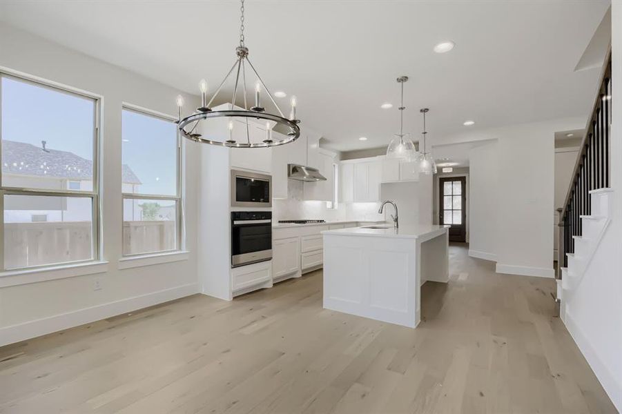 Open-concept living area featuring light wood-finish flooring and a contemporary chandelier
