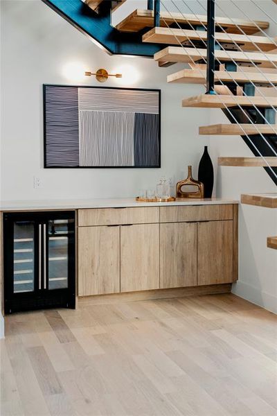 Bar featuring light wood-type flooring, beverage cooler, and light brown cabinetry