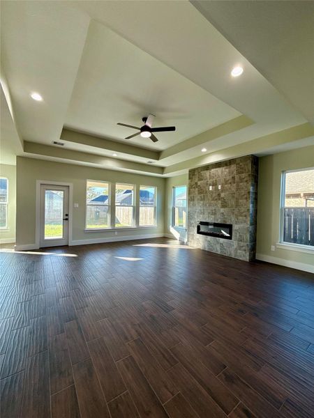 Spacious, sunlit living room with elegant wood tile flooring, modern recessed lighting, and a stylish modern ceiling fan. Features a sleek stone-tiled fireplace and large windows offering backyard views. Spacious, sunlit living room with elegant wood tile flooring, modern recessed lighting, and a stylish modern ceiling fan. Features a sleek stone-tiled fireplace and large windows offering backyard views.