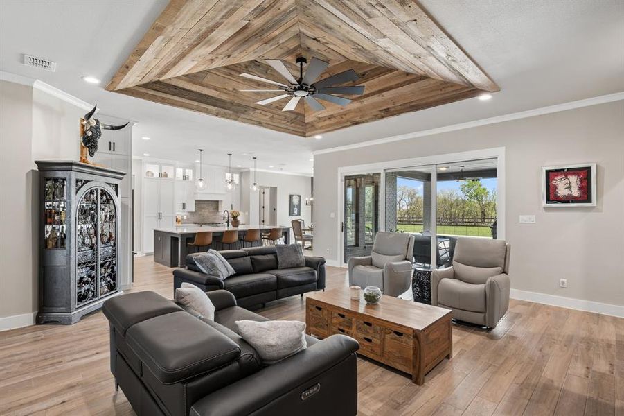 Living area with crown molding, light wood finished floors, a ceiling fan, a tray ceiling, and recessed lighting