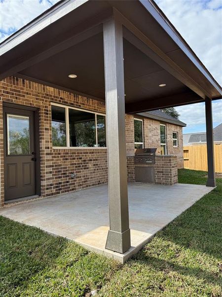 This is a modern brick home featuring a covered patio with a built-in grill, large windows, and a contemporary flat roof design. Ideal for outdoor entertaining.