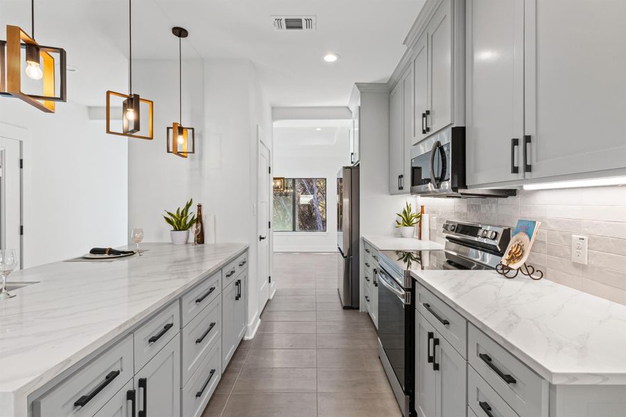 Kitchen featuring appliances with stainless steel finishes, light stone counters, pendant lighting, recessed lighting, and backsplash