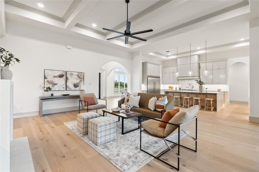 Living area with arched walkways, light wood-style floors, a ceiling fan, a tray ceiling, and recessed lighting Living area with arched walkways, light wood-style floors, a ceiling fan, a tray ceiling, and recessed lighting
