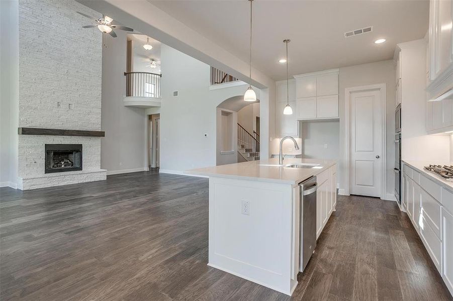 Kitchen featuring white cabinetry, an island with sink, a fireplace, ceiling fan, and sink