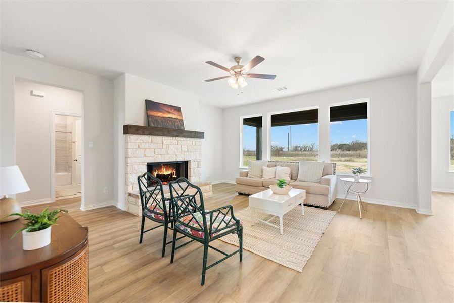 Living room with a stone fireplace, light wood-style flooring, and ceiling fan