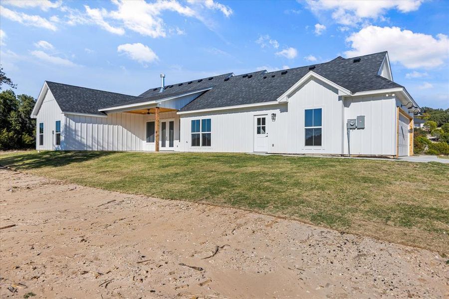 Back of house with roof with shingles, a patio, a yard, and board and batten siding