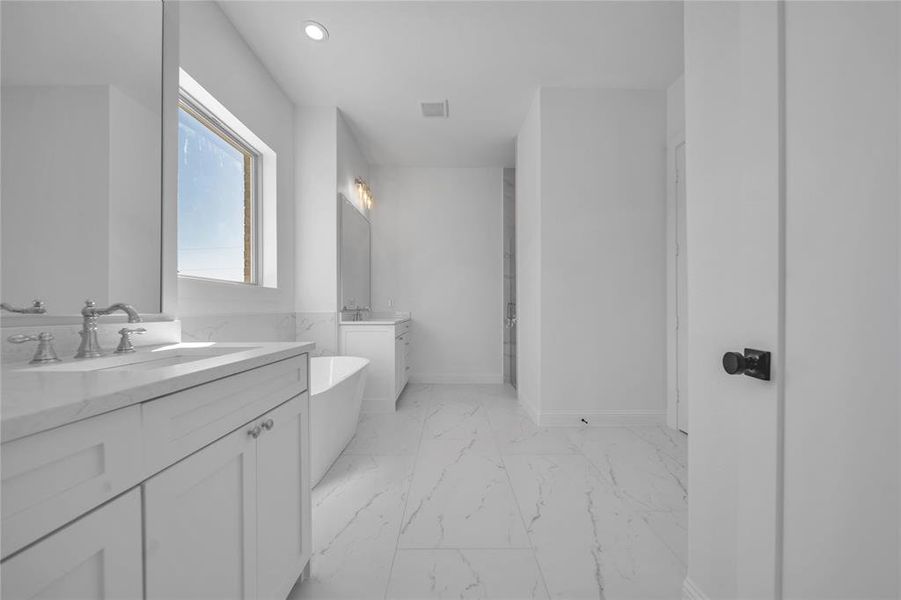 Bathroom with two vanities, a freestanding tub, light marble finish floors, and recessed lighting