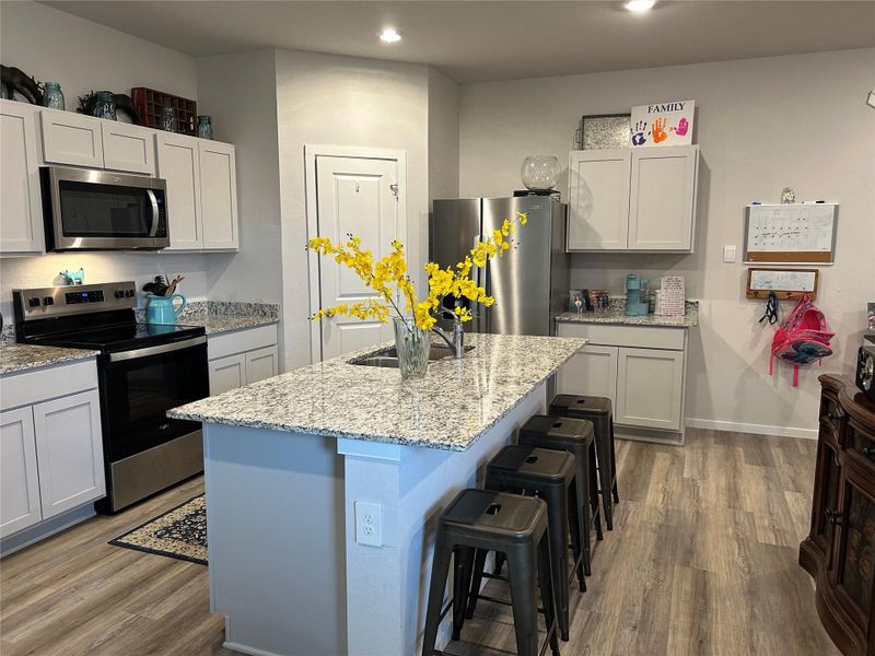 Modern kitchen featuring white cabinetry, granite countertops, stainless steel appliances, wood-finish flooring, and a central island with integrated seating