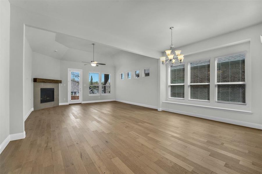 Unfurnished living room featuring a tile fireplace, a ceiling fan, suspended lighting, light wood-type flooring, and lofted ceiling