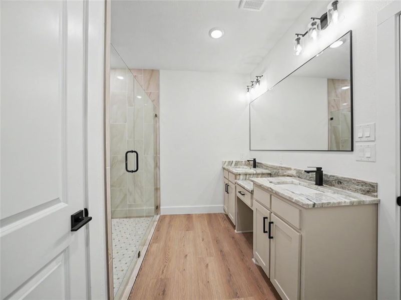 Spacious bathroom featuring a dual vanity with stone countertops, a large frameless mirror, and modern black fixtures Spacious bathroom featuring a dual vanity with stone countertops, a large frameless mirror, and modern black fixtures
