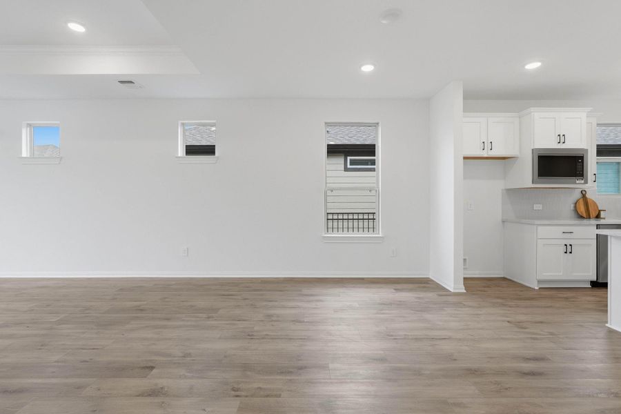 Bright, open-concept living and dining area with light flooring and recessed lighting, flowing into a modern kitchen with ample cabinetry and counter space, all filled with natural light.