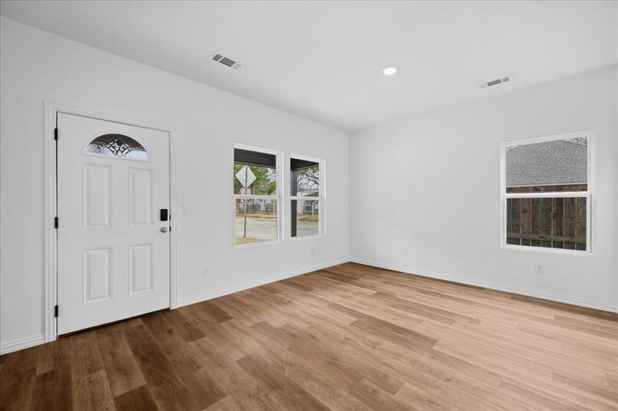 Bright living room featuring wood-look flooring, fresh neutral paint, recessed lighting, and abundant natural light from multiple windows. Clean, modern finishes throughout.