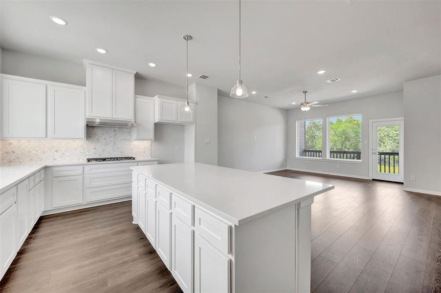 Open-concept kitchen featuring white shaker cabinetry, an expansive center island with a white countertop, and wood-finish flooring