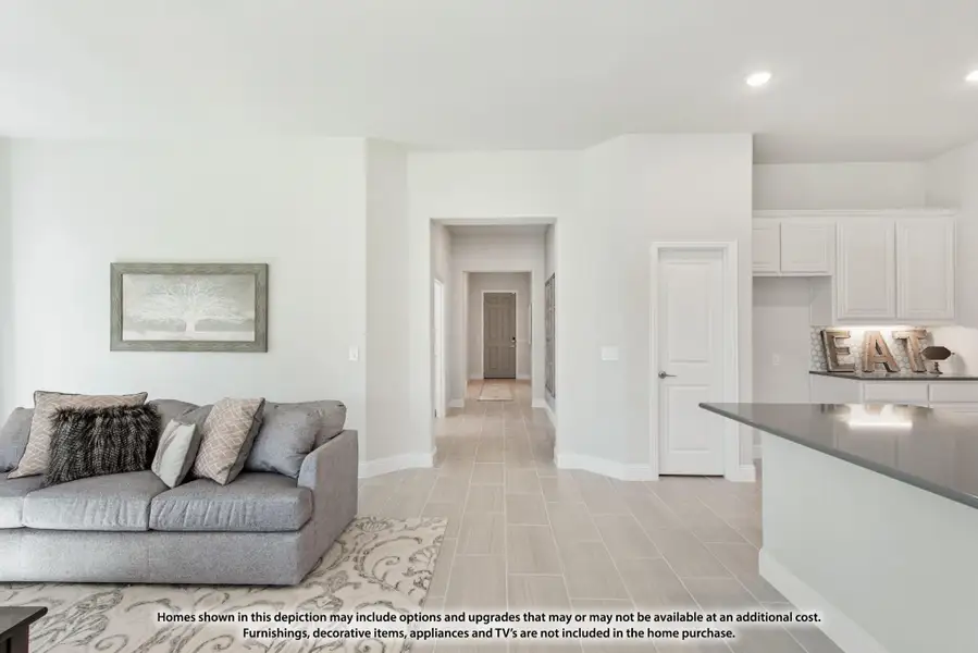 Open-concept living area with gray sofa, tile floors, and adjacent white kitchen cabinets visible Open-concept living area with gray sofa, tile floors, and adjacent white kitchen cabinets visible