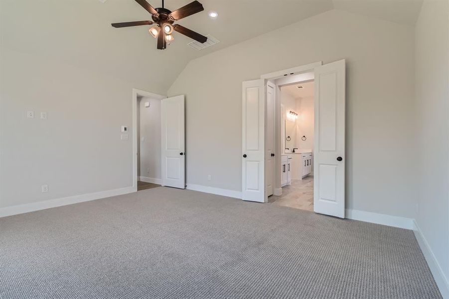 Unfurnished bedroom with connected bathroom, vaulted ceiling, light carpet, and ceiling fan