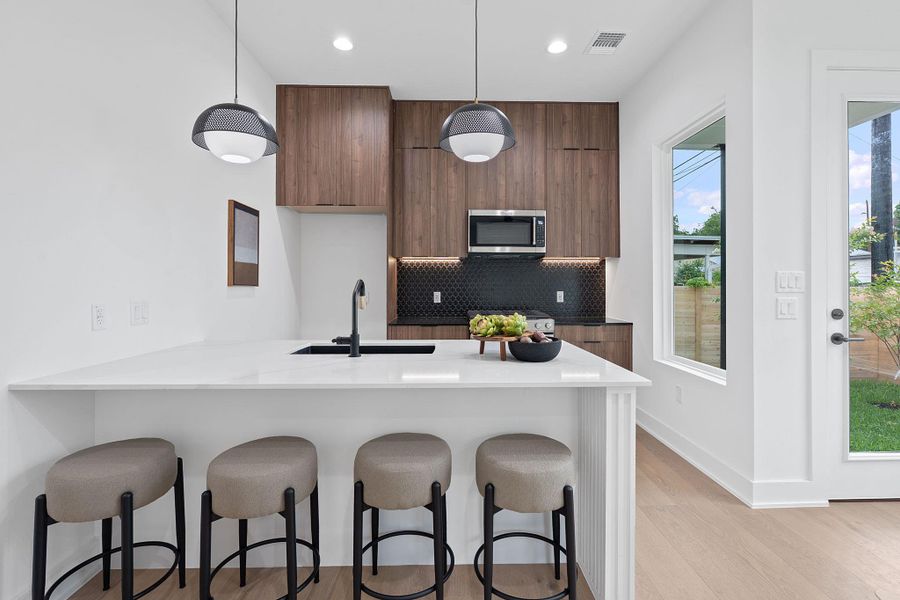 Kitchen featuring stainless steel microwave, modern cabinets, a breakfast bar, decorative backsplash, and recessed lighting