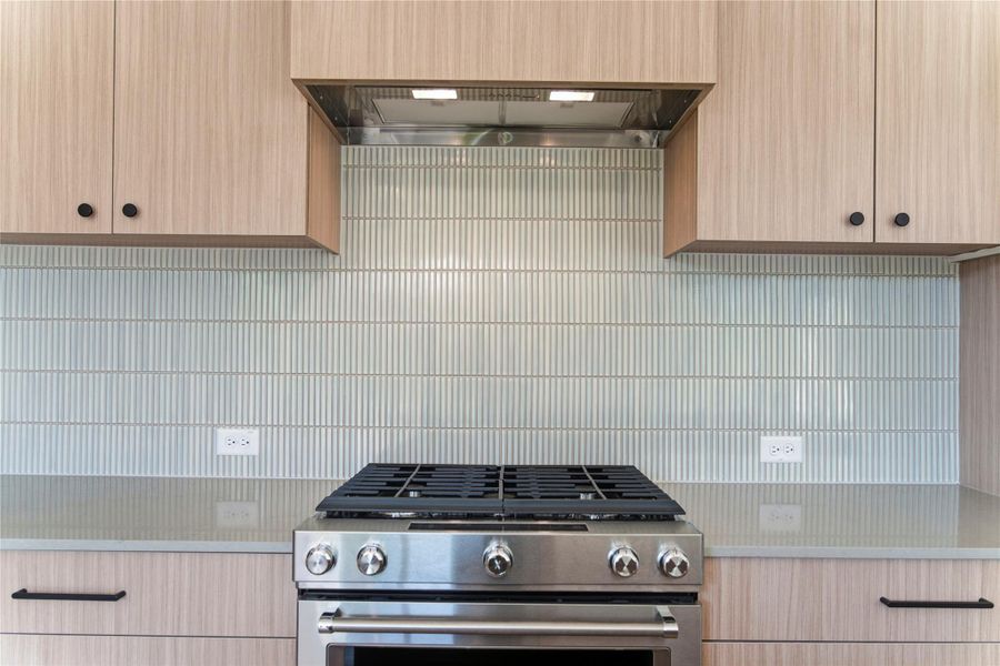 Kitchen with light brown cabinetry, high end range, wall chimney exhaust hood, and tasteful backsplash