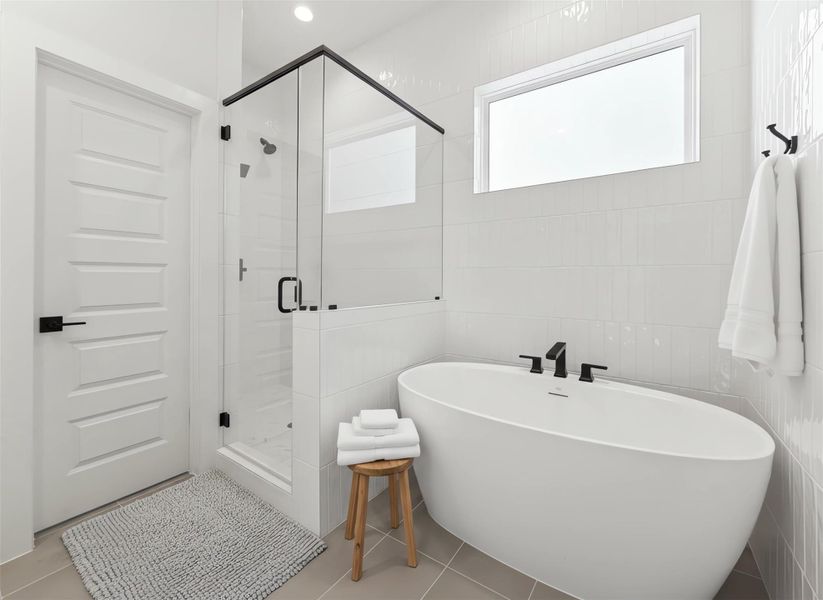 Primary bathroom features white tile, a soaking tub, and a glass-enclosed shower with a privacy barrier, creating a clean, spa-like retreat. *Virtually staged*