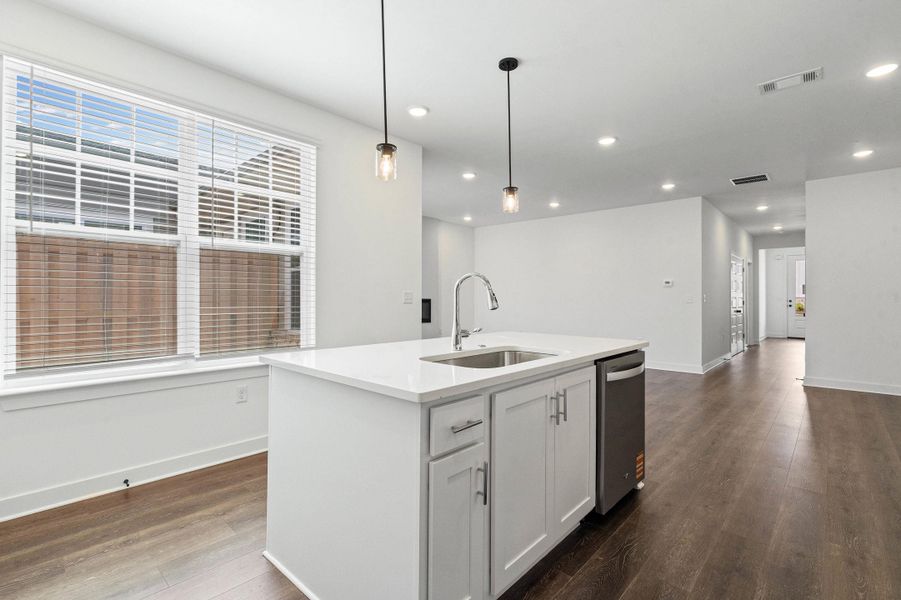 Kitchen island with a white countertop and a stainless steel sink, featuring pendant lighting and recessed ceiling lights