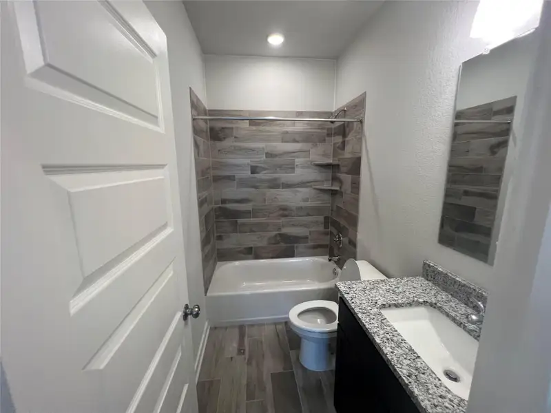 Modern bath with granite counters, tile flooring, and a tiled shower.