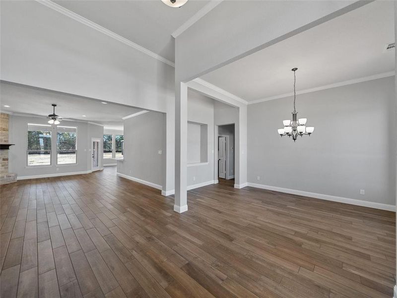 Prior listing photo. Property remains accurate - Unfurnished living room featuring crown molding, dark wood-type flooring, a chandelier, and ceiling fan