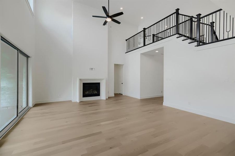 Spacious living area featuring high ceilings, wood-finish flooring, a contemporary fireplace, and a second-story overlook with black metal railings Spacious living area featuring high ceilings, wood-finish flooring, a contemporary fireplace, and a second-story overlook with black metal railings