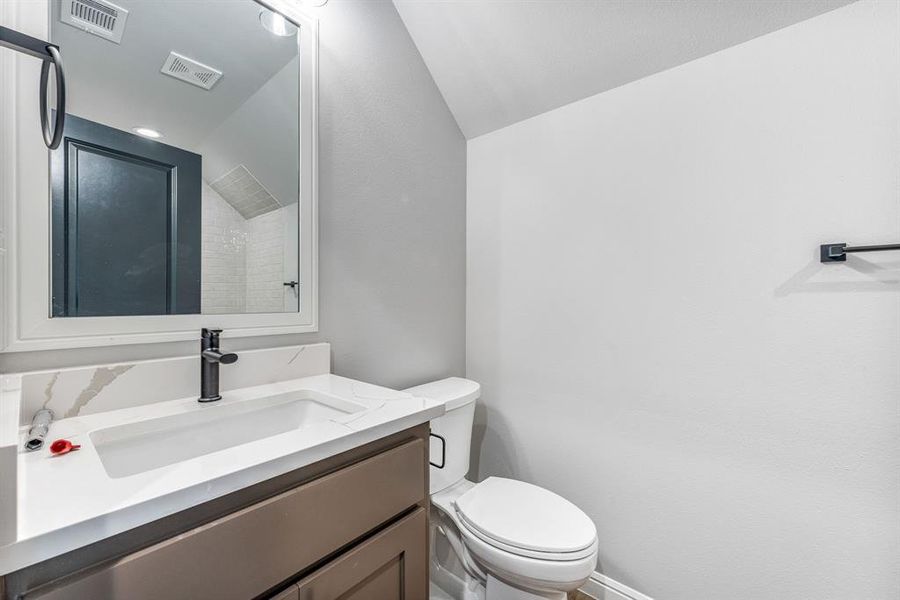 Bathroom featuring a shower, vanity, toilet, and vaulted ceiling