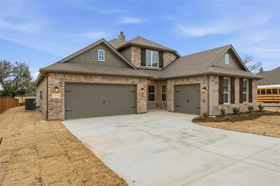 Craftsman inspired home featuring a shingled roof, an attached garage, driveway, and brick siding