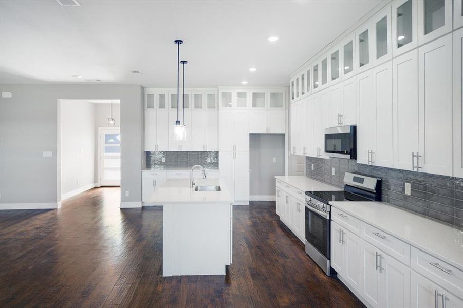Kitchen with backsplash, stainless steel appliances, white cabinetry, a kitchen island with sink, and dark wood-style flooring Kitchen with backsplash, stainless steel appliances, white cabinetry, a kitchen island with sink, and dark wood-style flooring