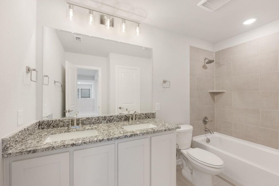Bathroom with double sink vanity, granite countertops, white cabinets, and tiled shower-tub combo Bathroom with double sink vanity, granite countertops, white cabinets, and tiled shower-tub combo