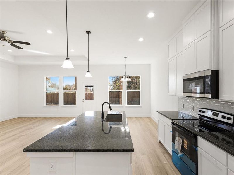 Kitchen featuring range with electric stovetop, dark stone countertops, white cabinetry, recessed lighting, and decorative light fixtures