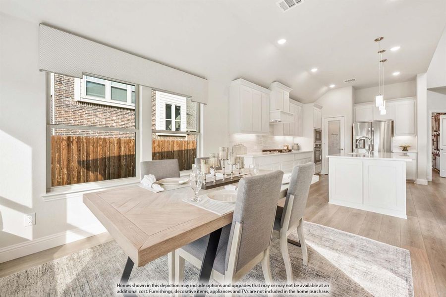 Open dining area with wood table flowing into white kitchen with island and hardwood floors