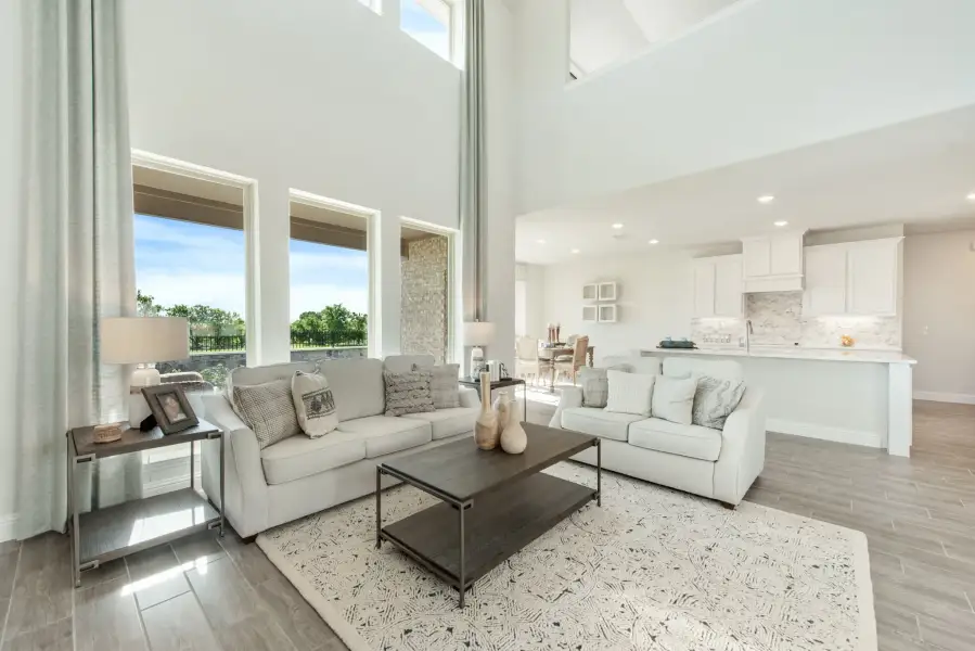 Open-concept living room with two-story ceilings, large windows, and view into white kitchen