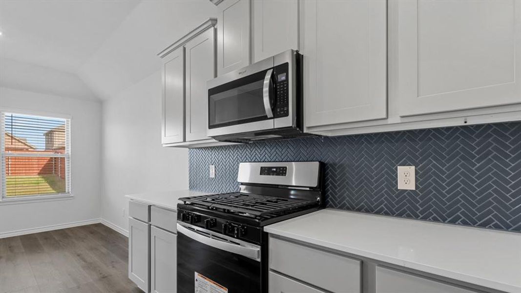 Kitchen with gas range oven, stainless steel microwave, backsplash, light wood finished floors, and light stone countertops