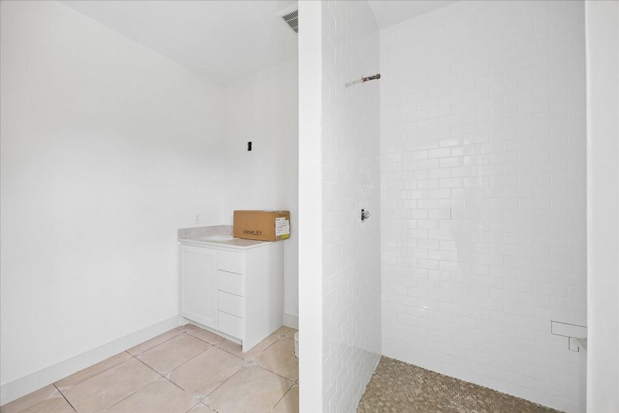 Bright and thoughtfully finished ensuite secondary bathroom featuring a walk in shower with clean white subway tile surround and contrasting pebble style shower floor. The vanity offers ample storage with soft close cabinetry and a neutral countertop, creating a fresh and functional space ideal for guests or everyday use.