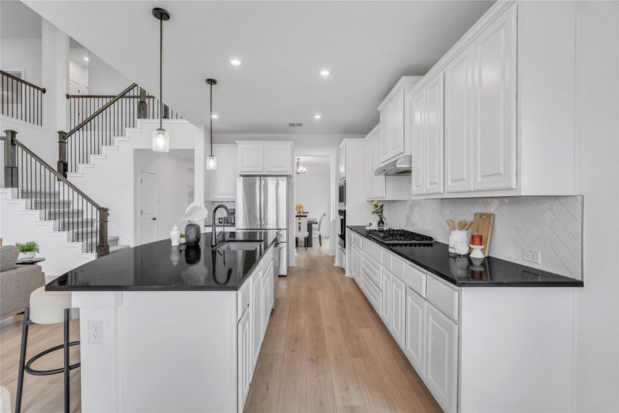 A luminous kitchen island with black countertops, pendant lighting, and light wood flooring invites culinary creativity.