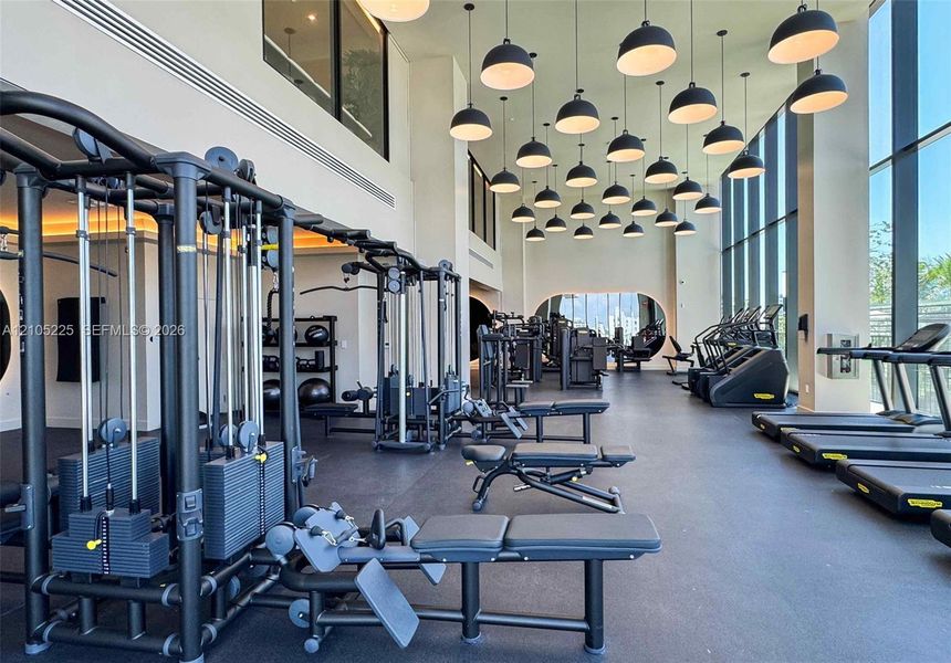 Fitness center featuring a high ceiling, extensive natural light from floor-to-ceiling windows, numerous pendant light fixtures, and varied exercise equipment